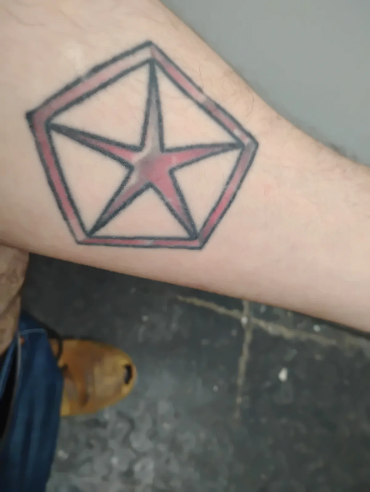 A close-up photo shows a tattoo on a person's forearm featuring a red five-pointed star enclosed within a black-outlined…