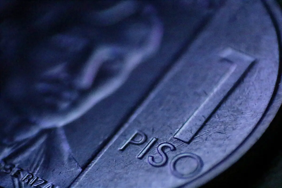 A close-up, blurry photograph of a Philippine 1-peso coin, showing the embossed number '1' and the word 'PISO' in focus…