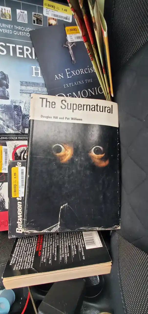 A stack of books on supernatural and paranormal topics sits on a car seat, with 'The Supernatural' by Douglas Hill and Pat…