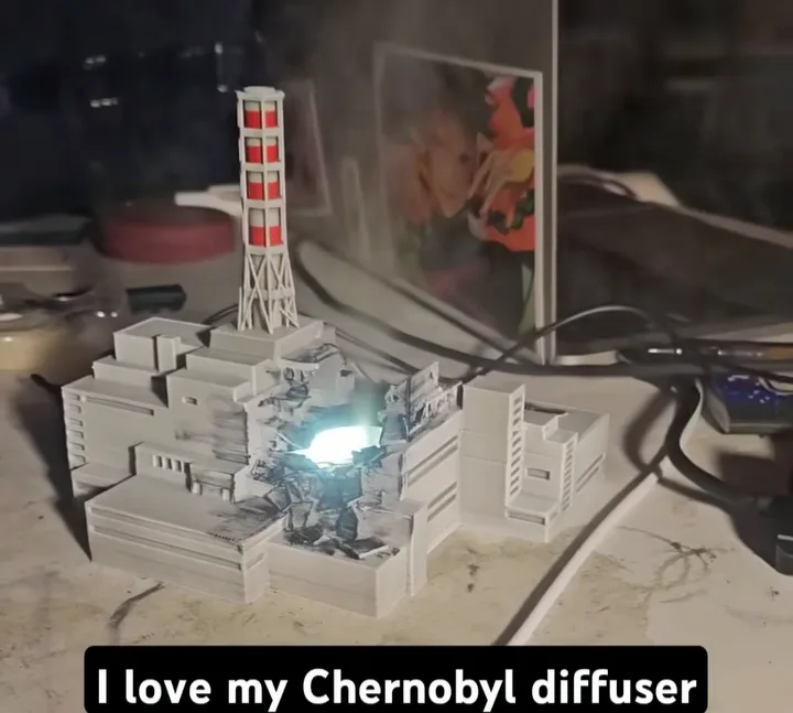 A 3D-printed model of the Chernobyl nuclear power plant is shown on a desk, with a bright blue light emanating from its…
