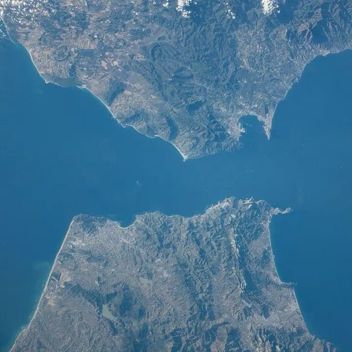 a satellite image shows two landmasses separated by water, forming a shape resembling the bat symbol from the Batman logo…