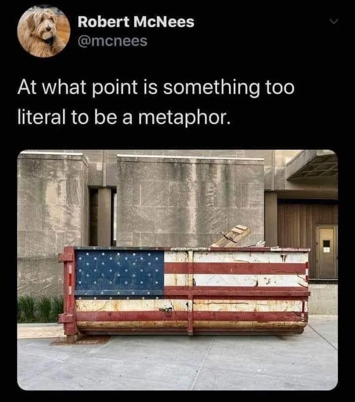 A weathered, rusty dumpster painted with the American flag is shown in front of a stone building. The overlaid text reads…