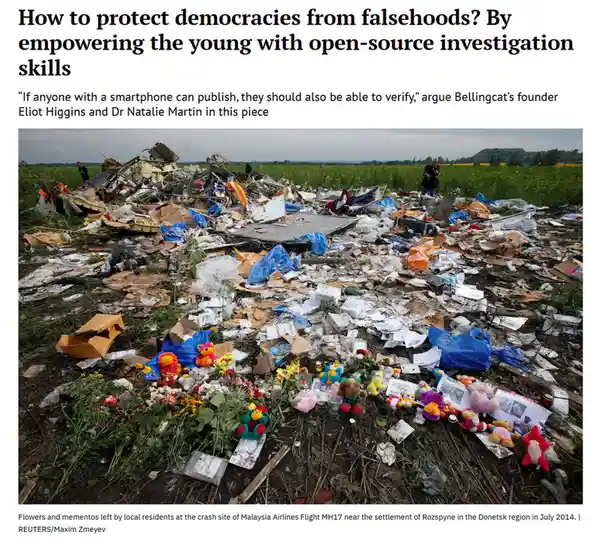 The image shows the wreckage of Malaysia Airlines Flight MH17 scattered across a field, with flowers and stuffed toys placed…