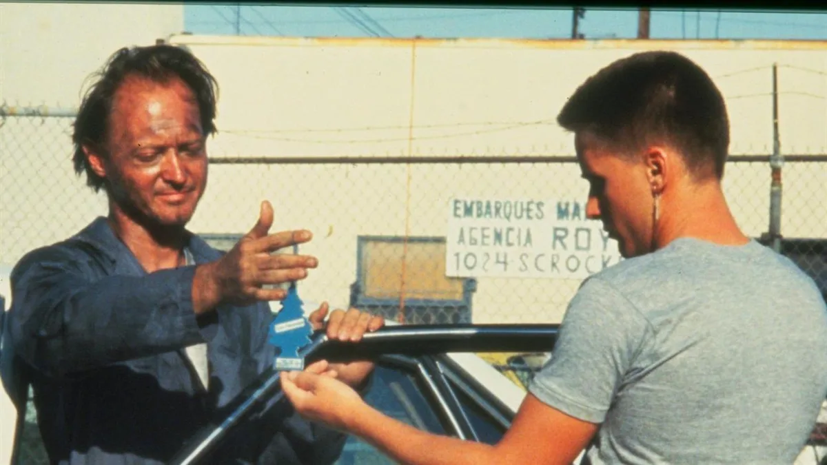 Two men are shown in a scene from the movie 'The Big Lebowski' where one man, wearing a blue shirt, is handing a blue air…