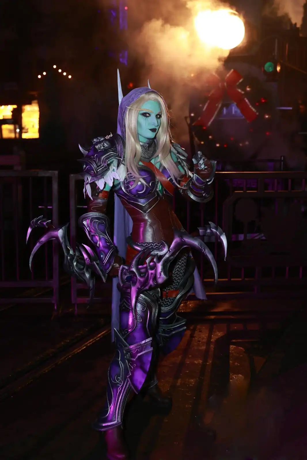 A person in elaborate fantasy cosplay, resembling a blue-skinned orc or night elf warrior with purple armor and clawed…