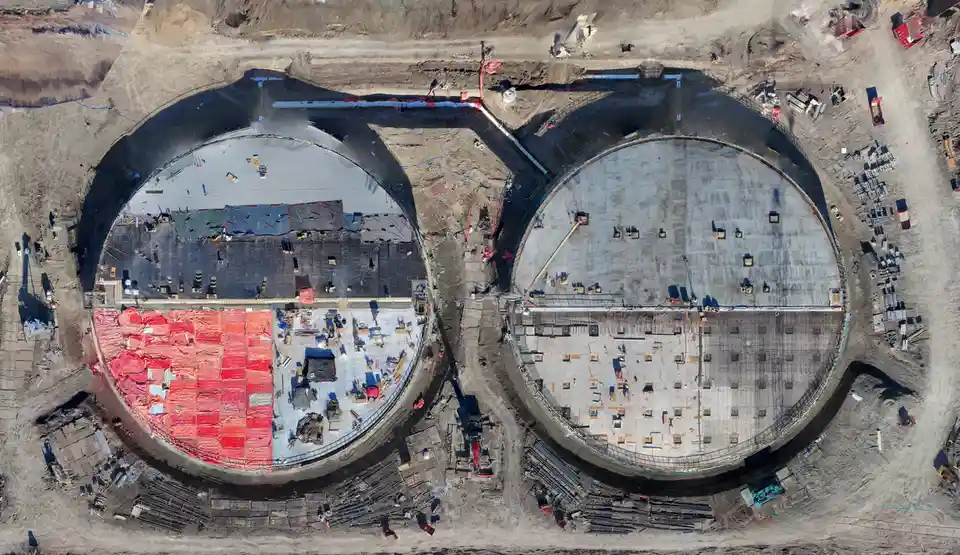 An aerial view of two large, circular construction sites with exposed concrete floors and scattered equipment. The left…