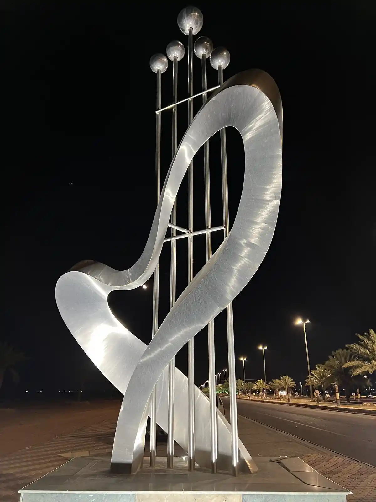 a large, illuminated, metallic sculpture at night, shaped like the letter 'y' with a curved top and vertical rods ending in…