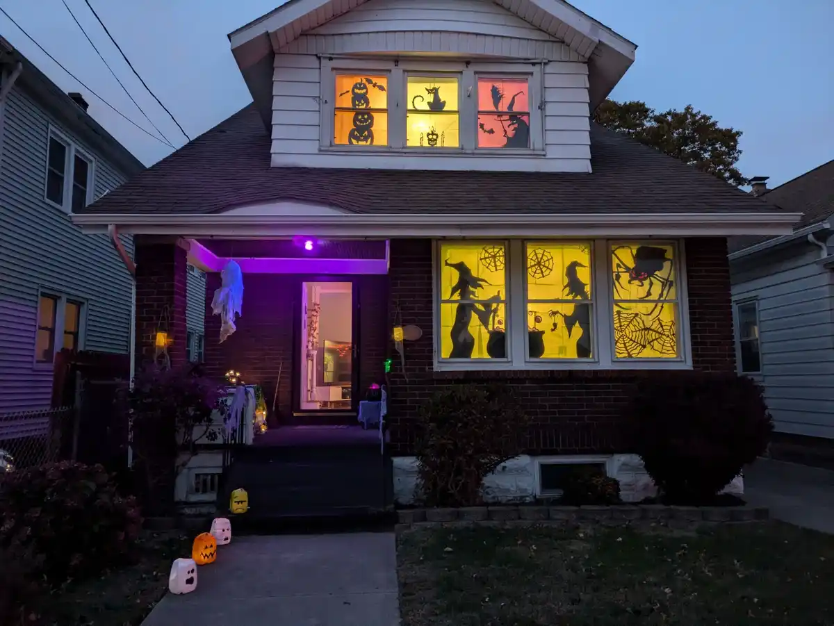 A house decorated for Halloween with spooky silhouettes of pumpkins, witches, and spiders visible through illuminated…