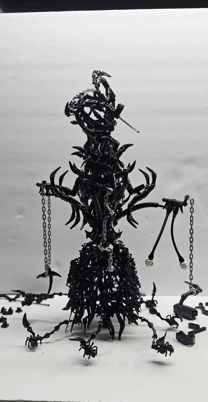 A towering, intricate sculpture made entirely of black LEGO pieces, resembling a monstrous, multi-limbed creature with…