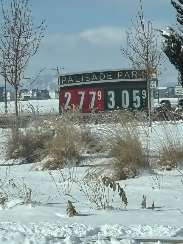 A snowy outdoor scene features a large sign for 'PALISADE PARK' with two sets of numbers: '2779' on a red background and…