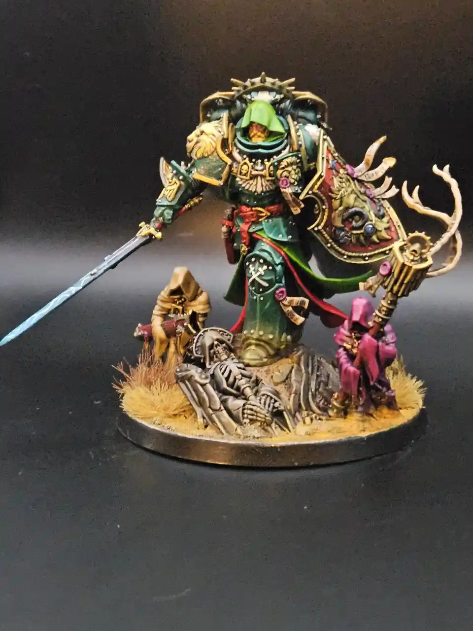 A highly detailed, painted miniature of a large, armored warrior in green and gold armor, holding a sword and a staff with…