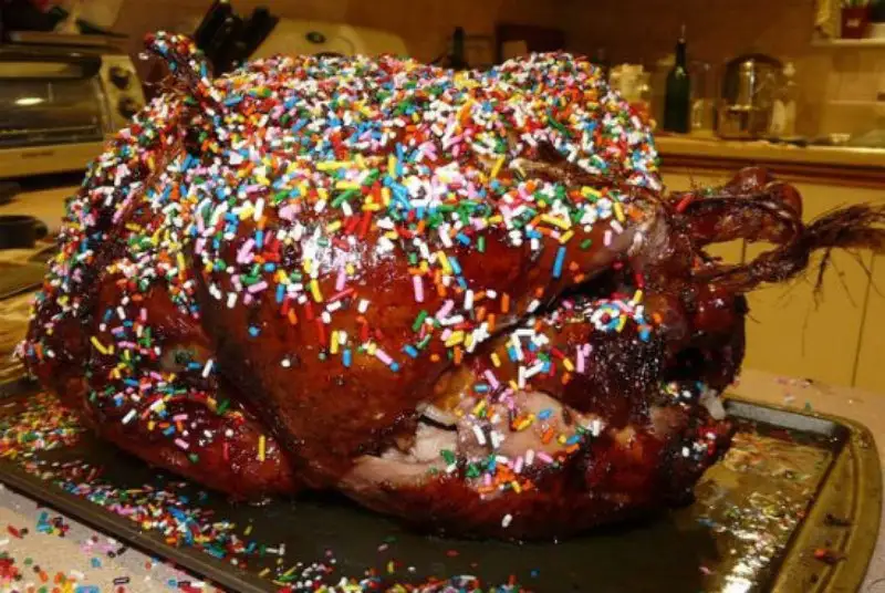 a roasted turkey with a glossy, dark brown skin sits on a metal baking tray, completely covered in multicolored, cylindrical…