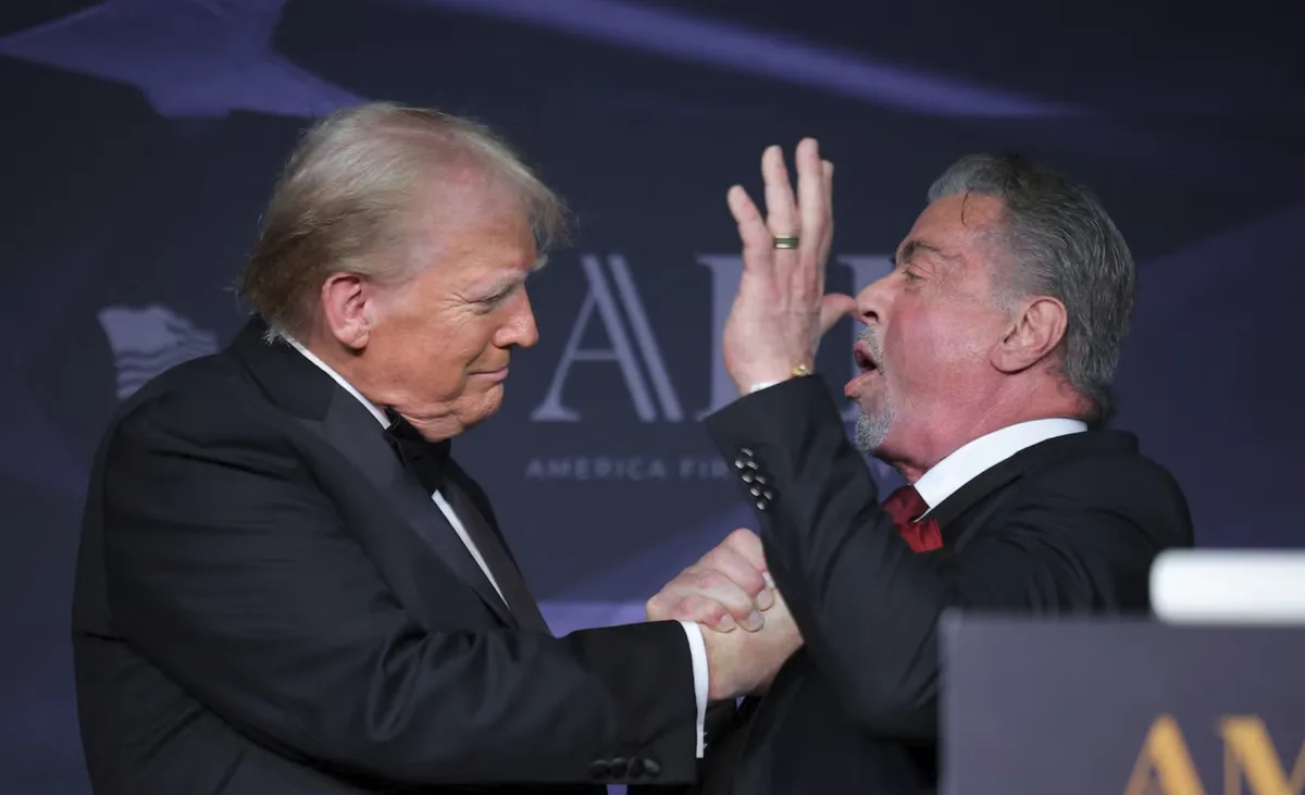 two men in formal suits, one with blonde hair and the other with gray hair, are shaking hands while the gray-haired man…