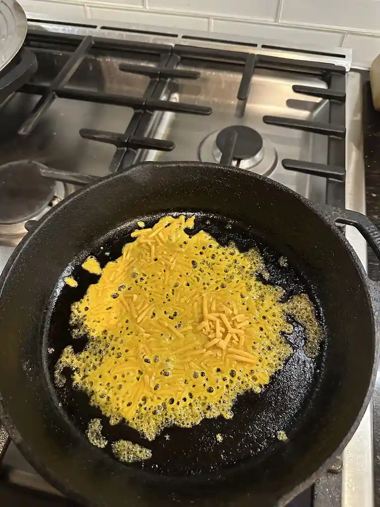 A black cast iron skillet sits on a stainless steel gas stove burner, containing a bubbling, melted yellow substance that…