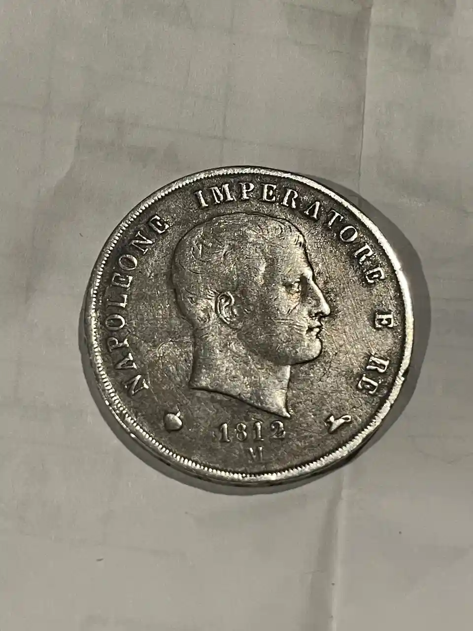 A close-up photo of a silver coin featuring a profile of Napoleon Bonaparte, with the text 'NAPOLEONE IMPERATORE E RE' and…