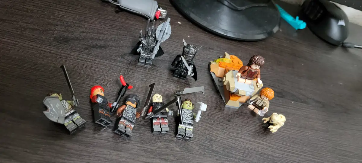 A photo of several lego minifigures on a dark wooden desk, depicting a scene from lord of the rings where hobbits frodo and…