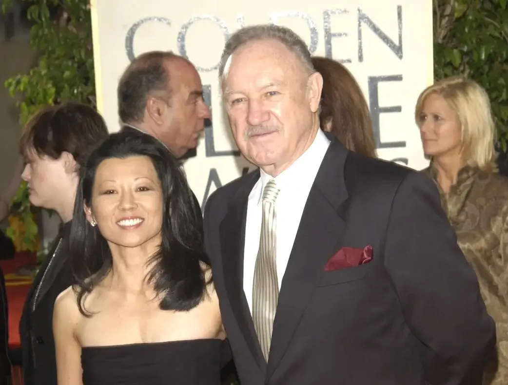 A man and woman pose together at a Golden Globe Awards event, smiling for the camera. The man, wearing a suit with a striped…