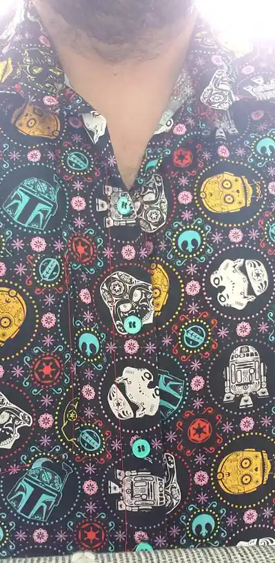 A close-up of a person wearing a black button-up shirt with a colorful pattern featuring Star Wars characters like Boba Fett…