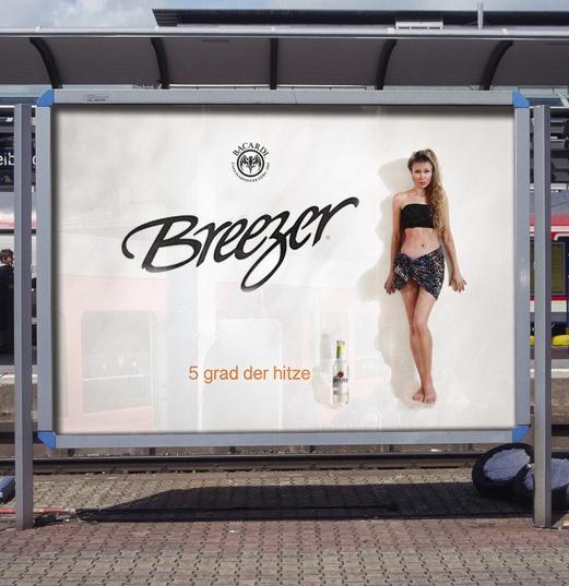 A bus stop billboard for Bacardi Breezer shows a woman in a bikini standing next to a bottle, with the text '5 grad der…