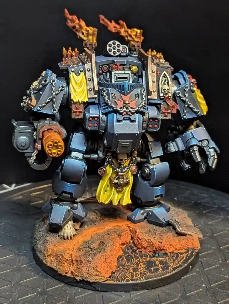 A heavily armored, blue-and-gold painted war machine with flaming cannons on its shoulders, skulls and chains, and yellow…