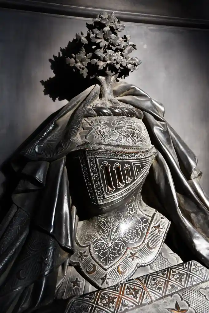A close-up of an ornate, dark metal statue of a knight in armor, with a detailed oak tree growing out of the top of its…