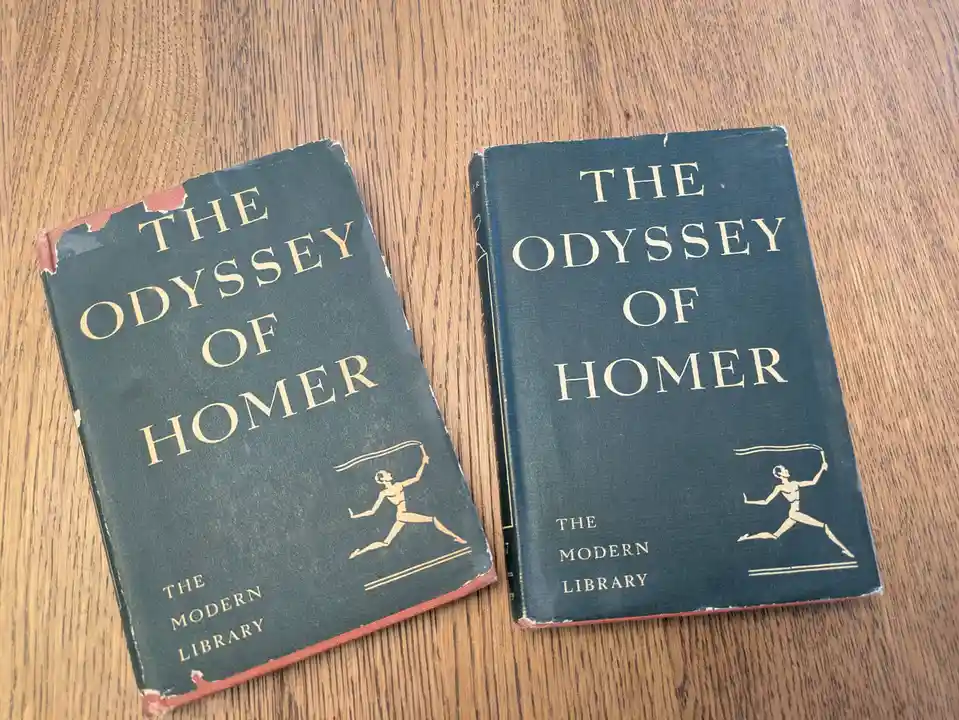 Two identical-looking dark blue hardcover books titled 'The Odyssey of Homer' from 'The Modern Library' series sit side by…