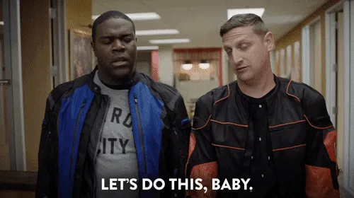 The image shows two men in matching black and blue jackets standing in a hallway. The man on the left repeatedly says 'LET'S…