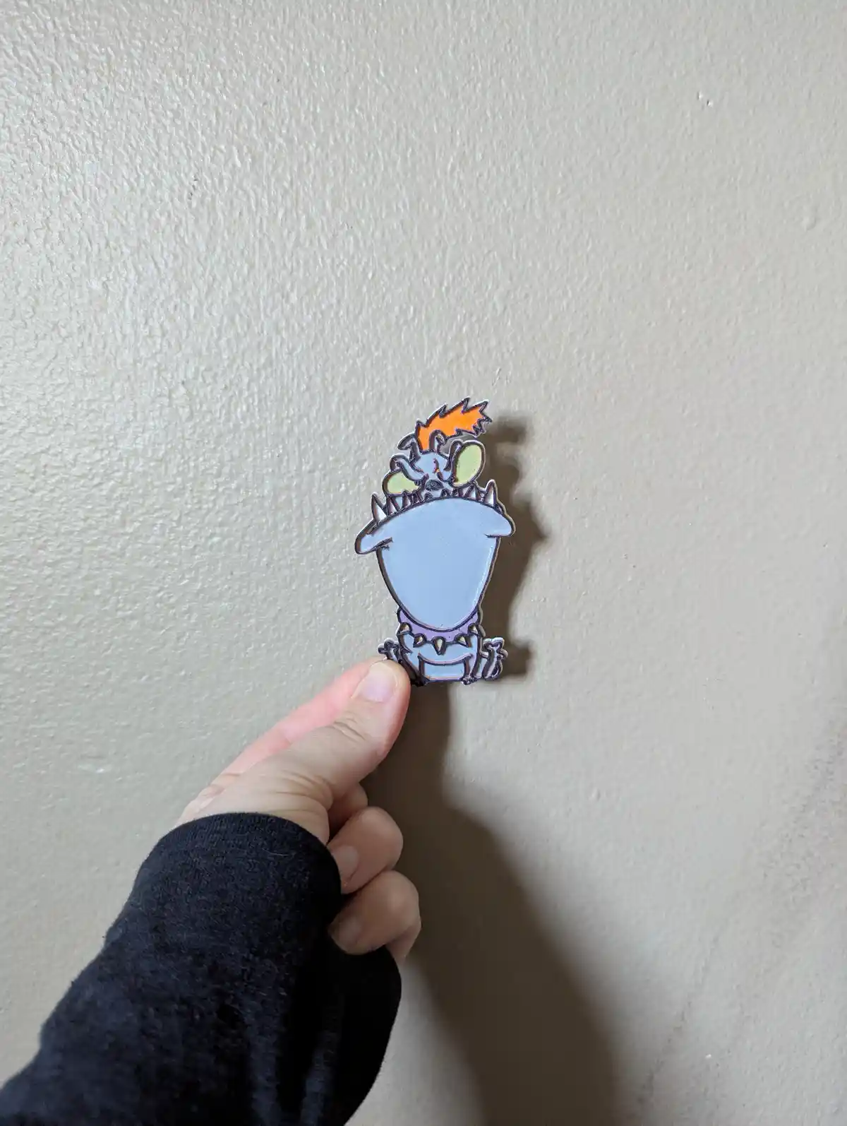 A hand holds up a small enamel pin featuring the cartoon character 'Squidward' from SpongeBob SquarePants, depicted with his…
