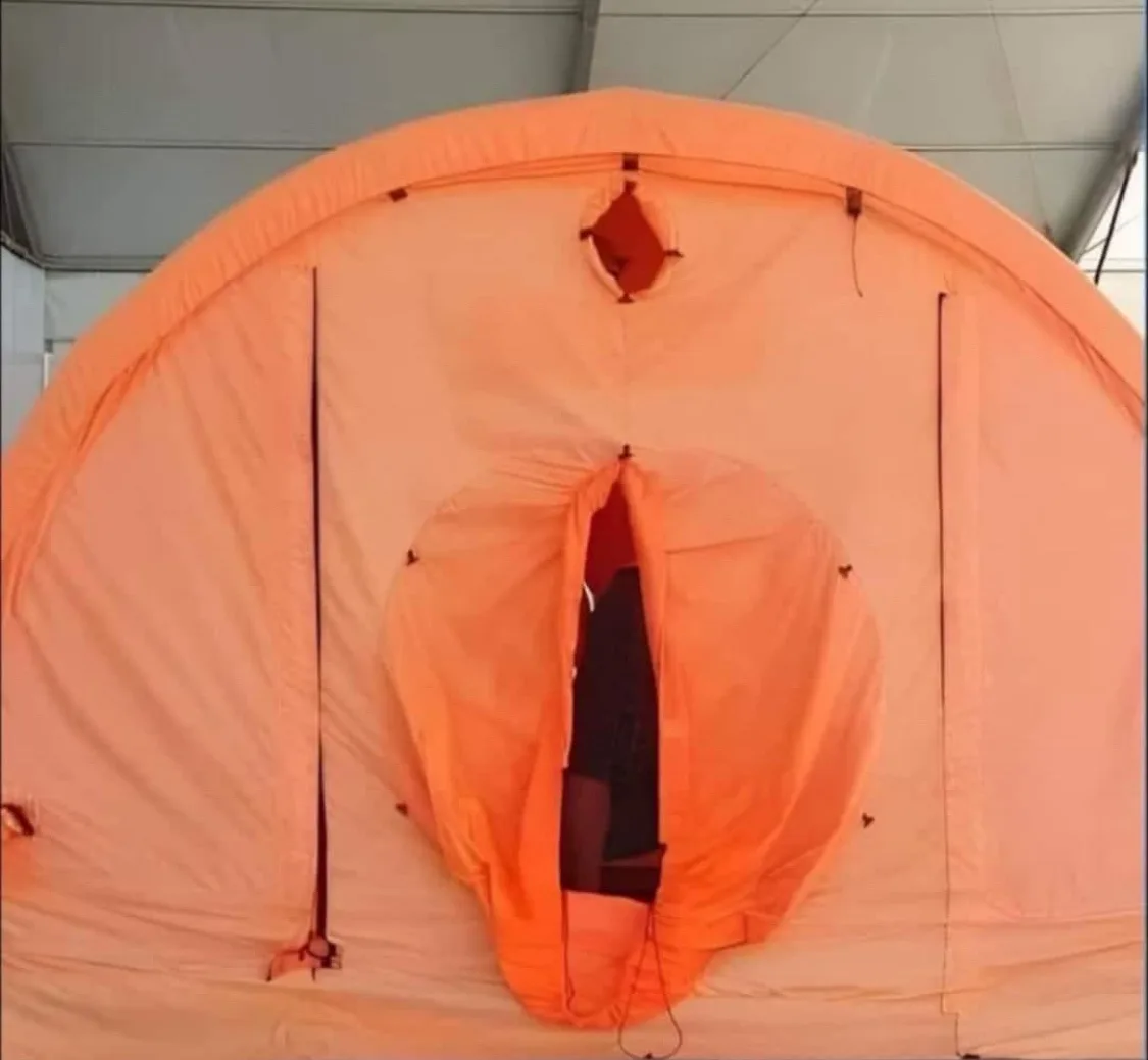 An orange dome tent with its entrance partially open, revealing a person inside. The tent's design, with a circular opening…