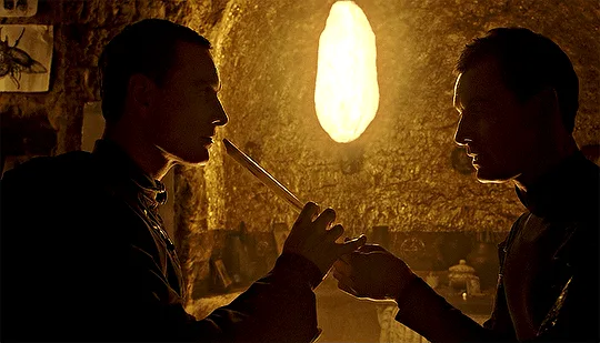 The image shows two men in a dimly lit, warmly lit room with stone walls and hanging lamps. In a sequence of panels, one man…