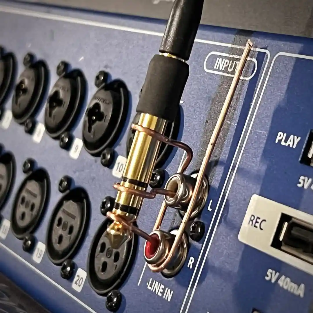 A close-up photo of an audio jack plugged into a blue device's 'LINE IN' port, with a copper wire visibly soldered to the…
