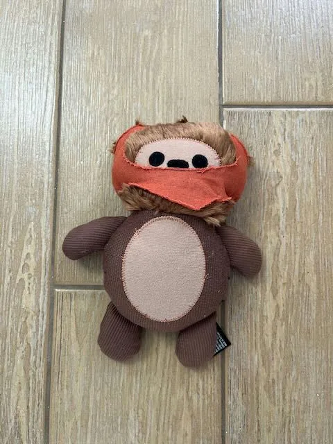 A small, handmade plush toy resembling a Wookiee from Star Wars, featuring brown fur, an orange head covering, and a round…