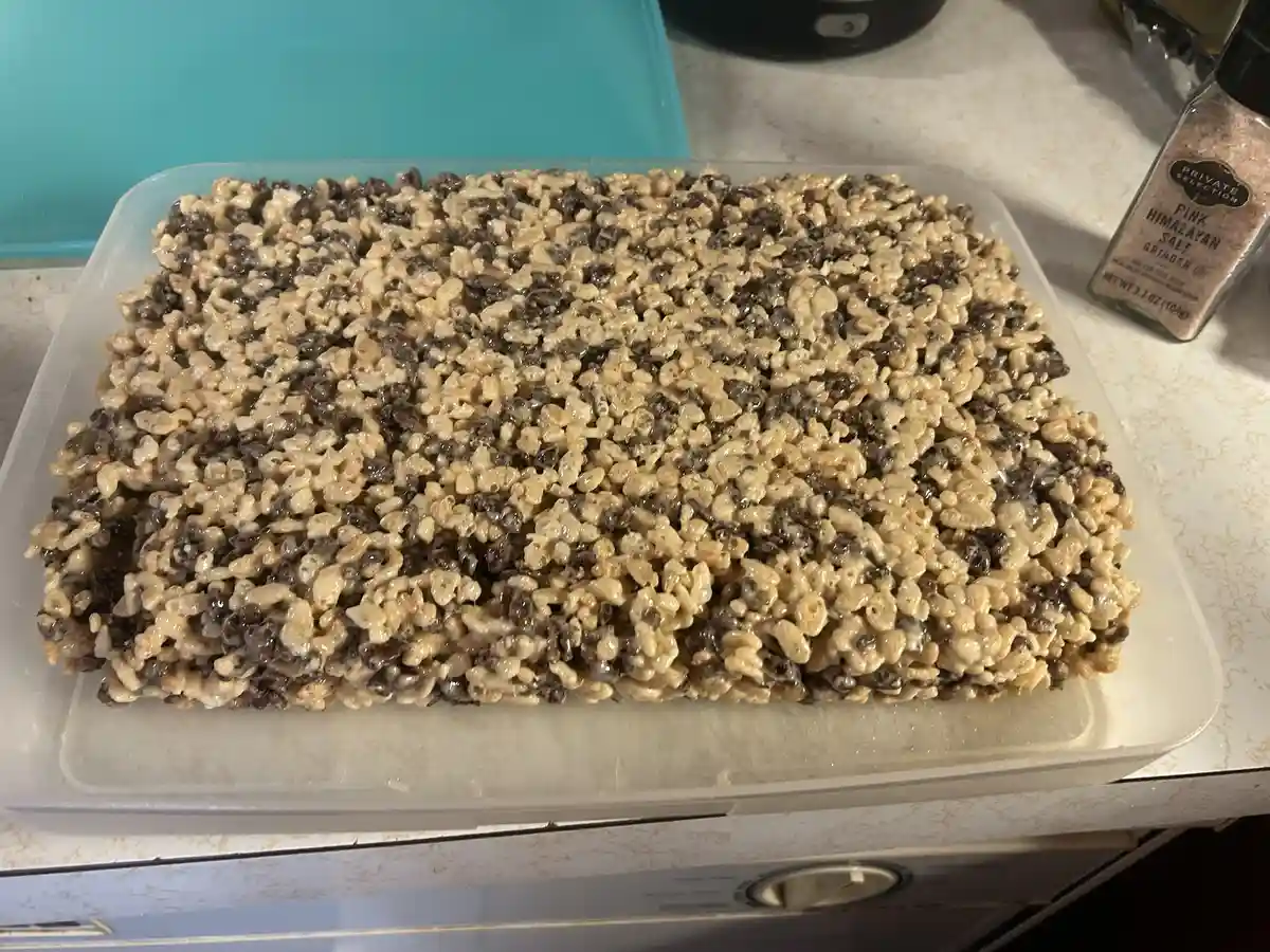 A rectangular pan of homemade rice krispies treats with chocolate chips, showing a distinct pattern of dark and light…
