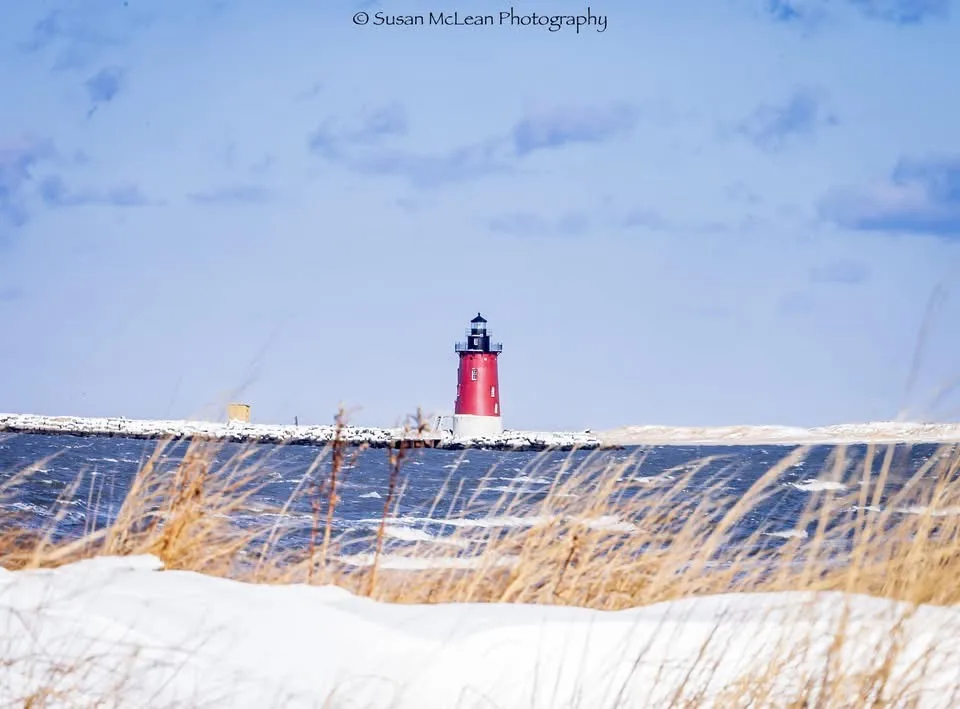 A scenic photograph shows a red and white lighthouse standing on a snow-covered pier extending into a choppy, icy blue sea…