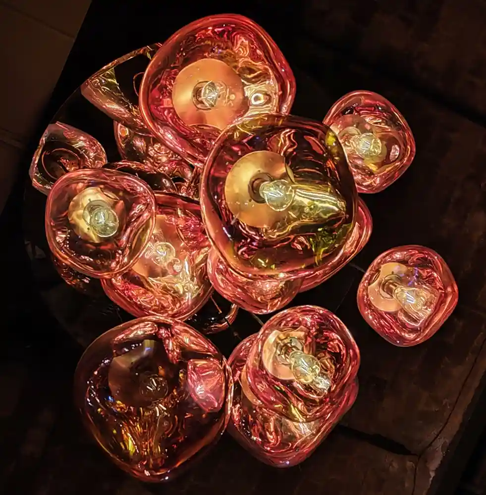 a close-up photo of a modern, artistic chandelier composed of multiple irregular, translucent glass orbs in shades of red…