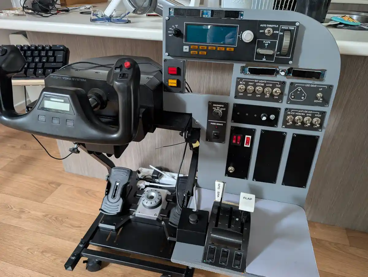A homemade flight simulator cockpit setup with a yoke, throttle quadrant, and panel of switches and dials, placed on a desk…