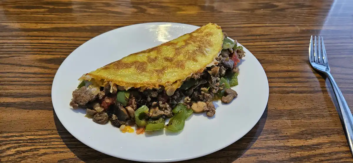 A close-up photo shows a folded, golden-brown omelette on a white plate, revealing a filling of ground meat, green peppers…