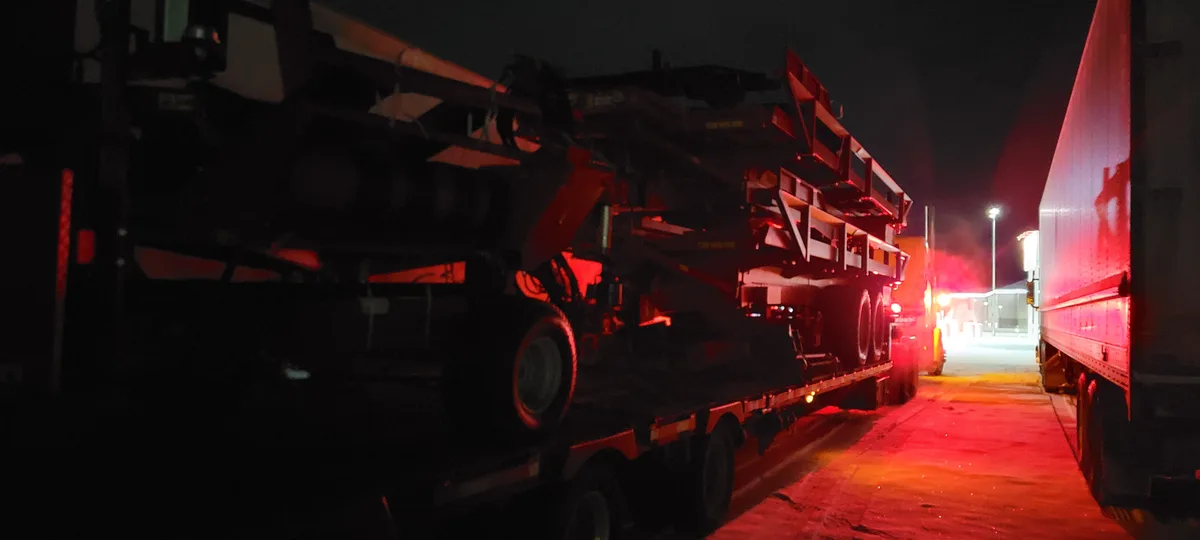 A nighttime photo shows a large, complex piece of heavy machinery, possibly a crane or construction equipment, mounted on a…