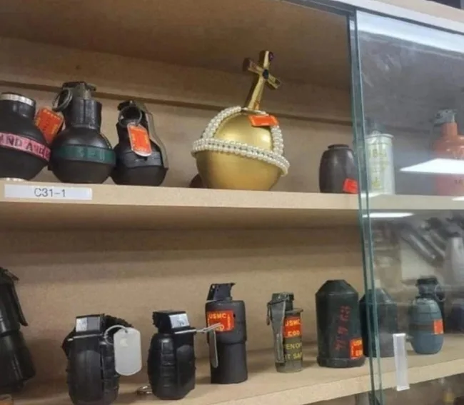 A museum display case shows various historical grenades on shelves, including black and green hand grenades with tags…