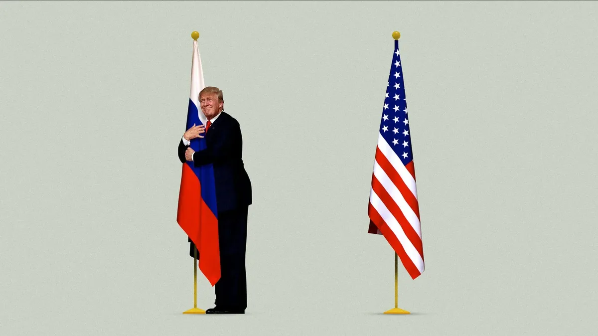 A man in a dark suit stands between two flags, one Russian and one American, smiling while embracing the Russian flag. The…