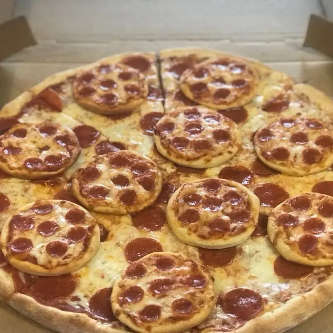 a close-up photo of a large pepperoni pizza inside an open cardboard box, with numerous small, round pepperoni pizzas placed…