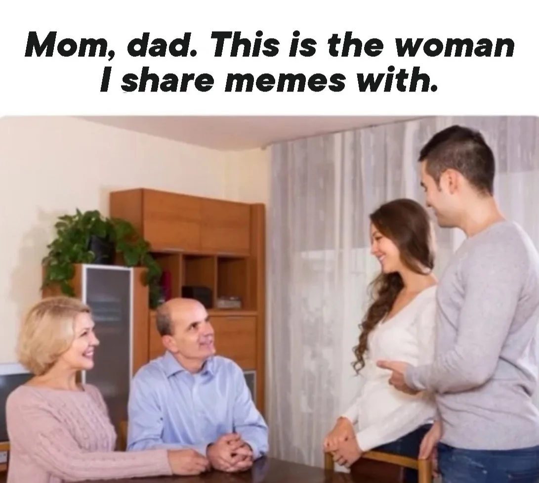 A man stands beside a smiling woman, pointing at her while introducing her to his parents, who are seated at a table and…