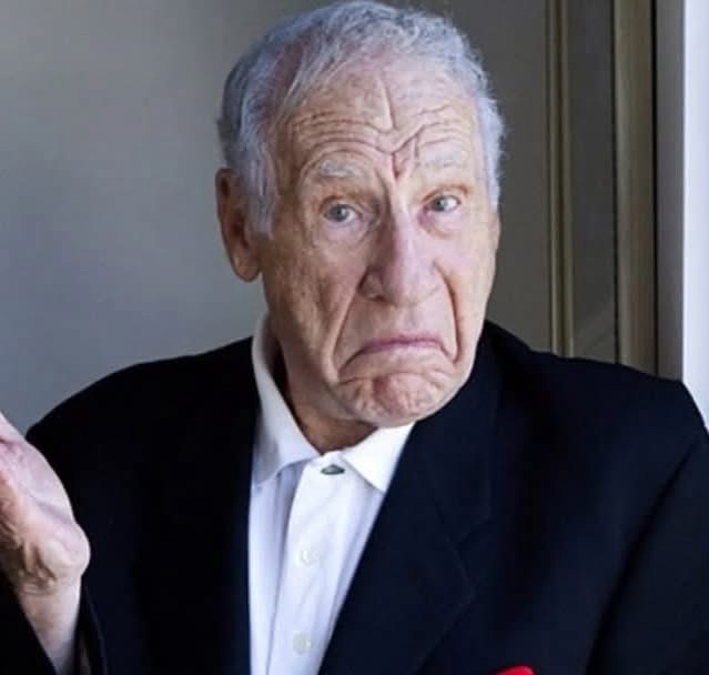 an elderly man with gray hair, wearing a black suit and white collared shirt, stares intensely at the camera with a deeply…