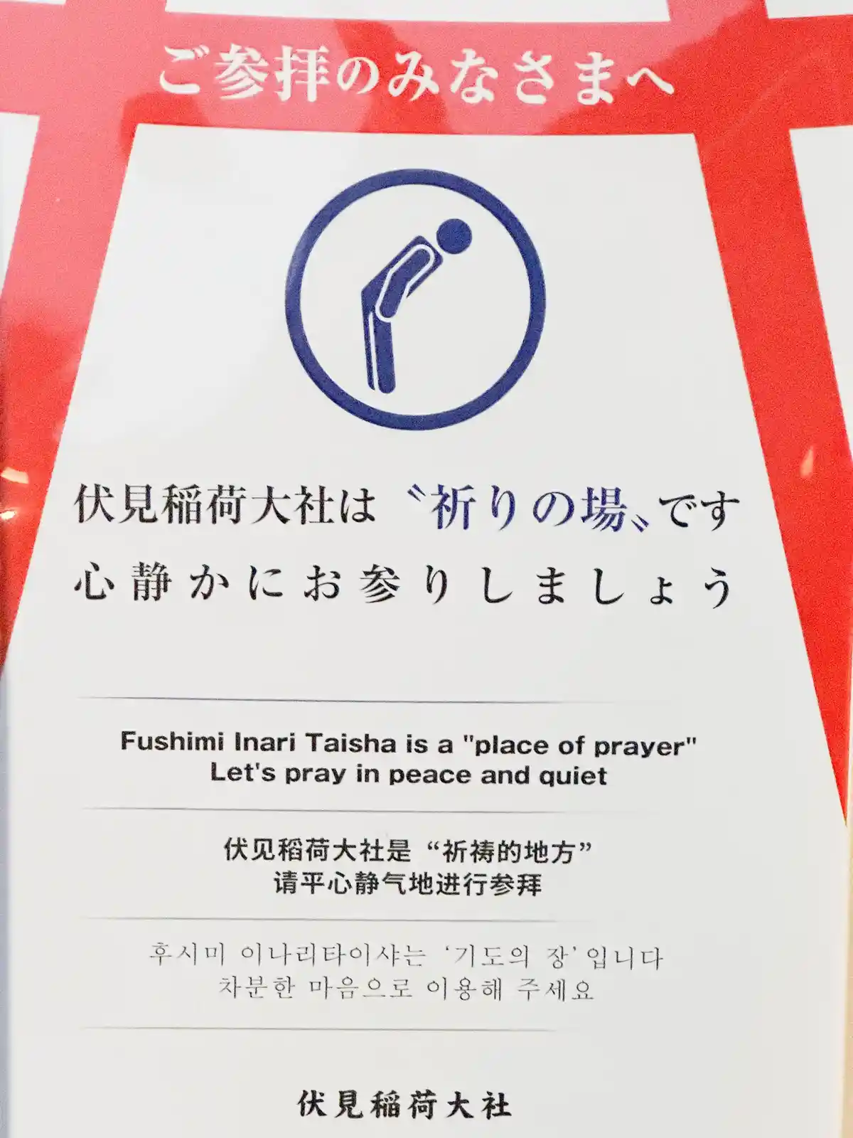 A sign at Fushimi Inari Taisha shrine in Japan, featuring a blue icon of a person bowing, with text in Japanese, English…