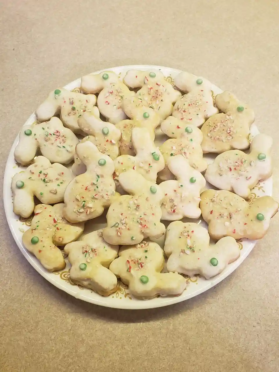 A white plate with gold trim holds numerous gingerbread cookies shaped like reindeer, covered in white icing, red and green…