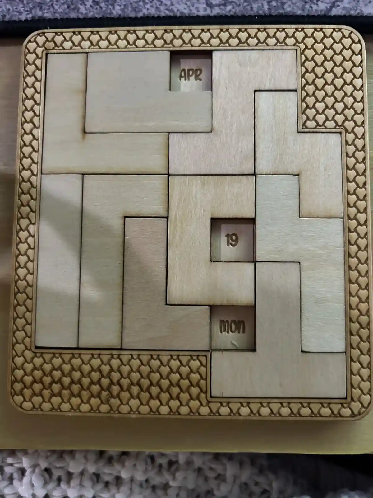 A wooden puzzle calendar with interlocking pieces, where three small squares are visible through gaps: one shows 'apr', one…