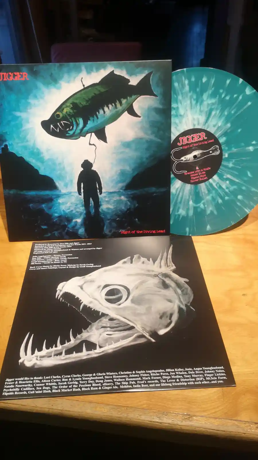 A vinyl record and its album art for 'Jigger - Night of the Diving Lead' are displayed. The front cover shows a menacing…