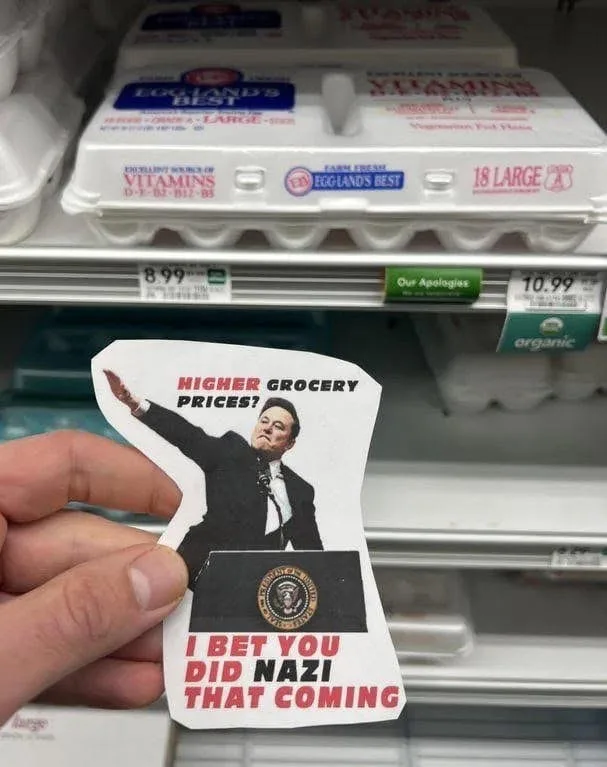 A hand holds a cutout of Donald Trump at a podium with the presidential seal, overlaid with the text 'HIGHER GROCERY PRICES?…