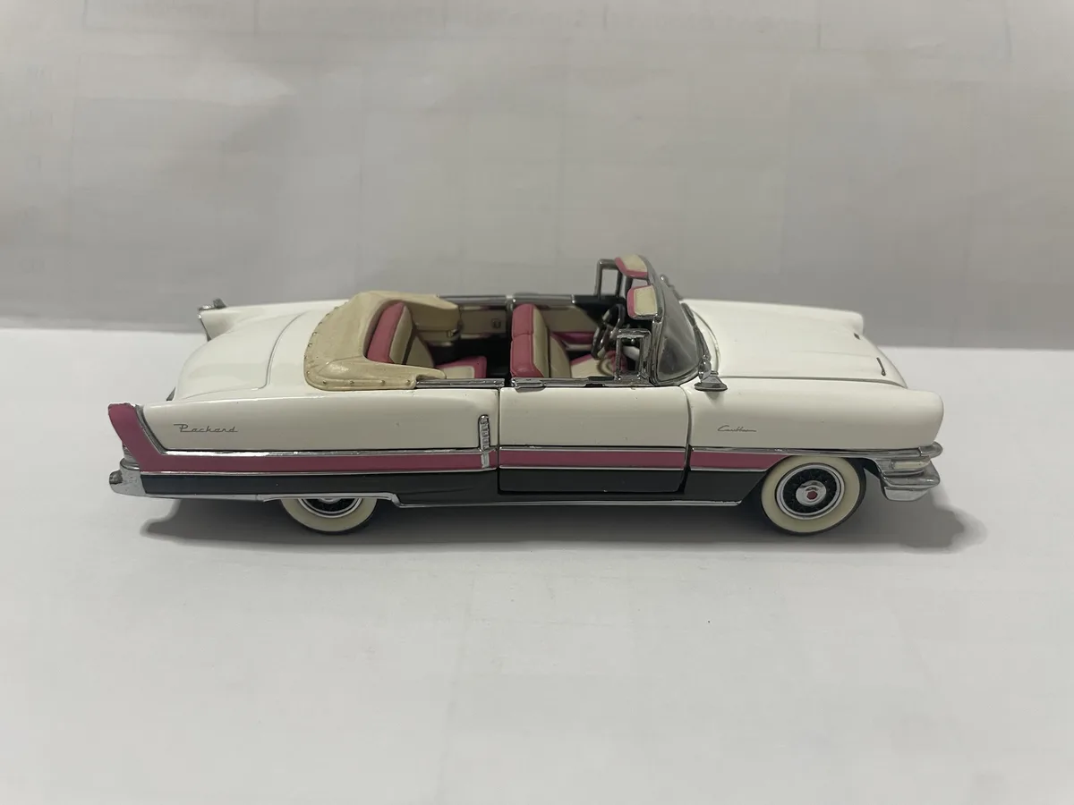A white and pink 1950s-style die-cast convertible toy car with chrome trim and a tan interior is shown from the side on a…