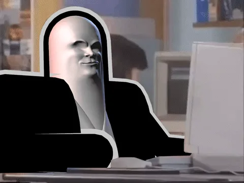 The image shows a bald, white-faced character with a stern expression sitting at a desk in front of a computer monitor. The…